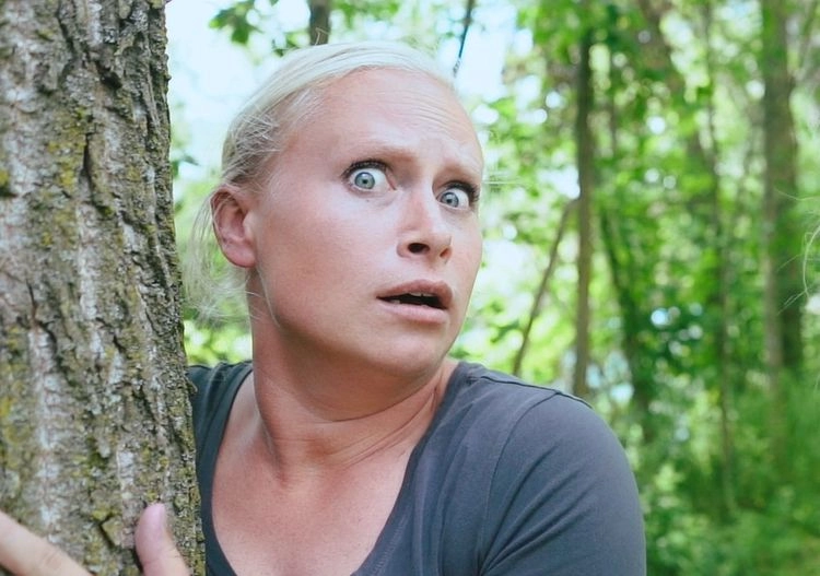Katie peeking wide-eyed from behind a tree